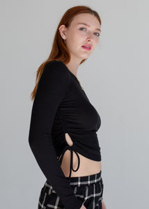 Woman wearing a black long-sleeve top and plaid pants on a gray background