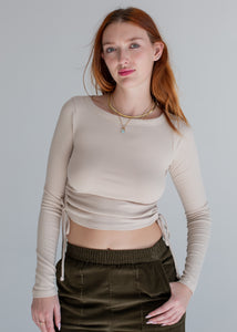 Woman wearing a beige long-sleeve top and green pants against a plain background