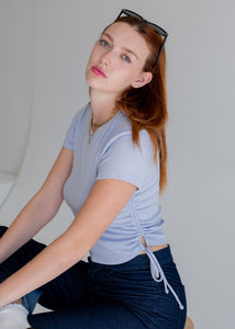 Woman sitting on a chair wearing a light blue shirt and dark pants with sunglasses on her head.