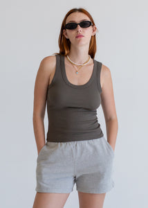 Woman wearing a dark grey tank top and gray shorts against a plain background