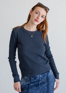 Woman wearing a navy blue long sleeve 
and jeans against a plain background