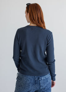 Person wearing a navy blue long sleeve and jeans on a plain background