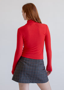 Person wearing a red sweater and plaid skirt on a plain background