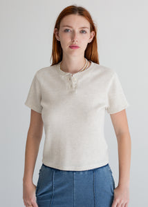 Woman wearing a beige short-sleeve shirt and blue jeans against a plain background