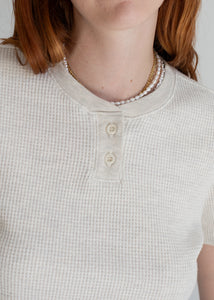 Person wearing a textured beige shirt with buttons and a pearl necklace.