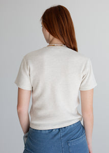 Person wearing a beige textured shirt and blue pants against a plain background