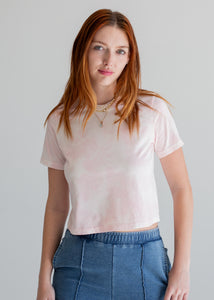 Woman wearing a light pink t-shirt and blue jeans against a plain background