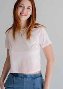 Woman wearing a light pink t-shirt and blue jeans against a plain background