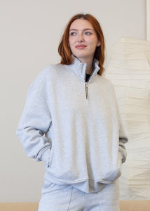 Woman wearing a gray zip-up sweatshirt in a minimal indoor setting