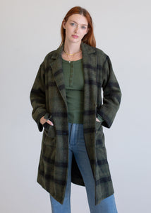 Woman wearing a green plaid coat over a green top and blue jeans on a white background