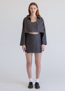Woman wearing a gray checkered outfit with a jacket, top, and skirt on a white background