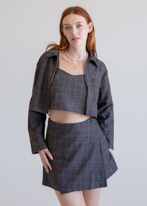Woman wearing a gray plaid outfit with a jacket, top, and skirt on a plain background