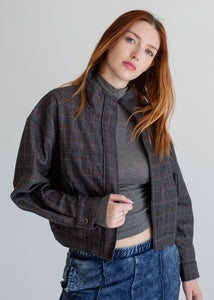 Woman wearing a plaid jacket over a gray top and blue jeans on a plain background