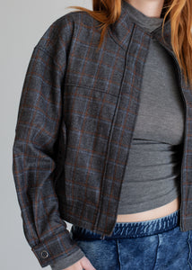 Person wearing a plaid jacket over a gray top and blue jeans on a plain background