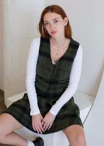 Woman wearing a green vest over a white long-sleeve shirt, sitting on a white chair.