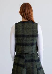 Person wearing a green plaid vest and skirt set on a plain background