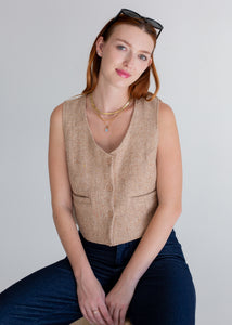 Woman wearing a beige vest and dark jeans against a plain background